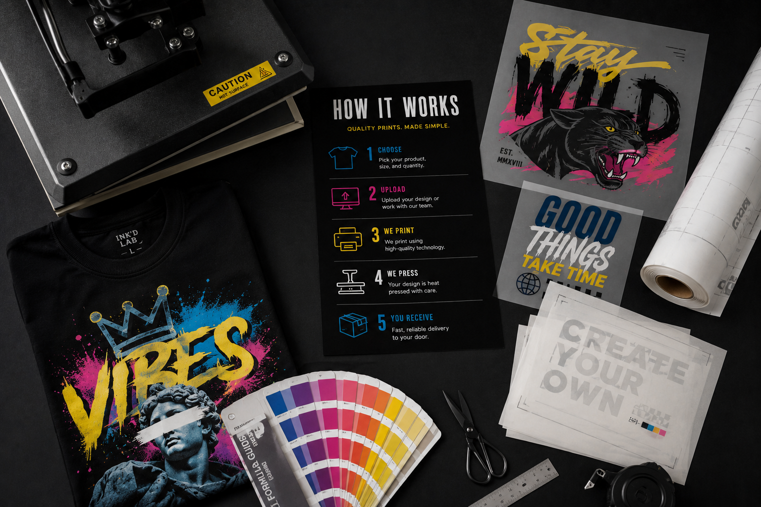 Print production workspace with heat press, color swatches, transfer sheets and finished garments